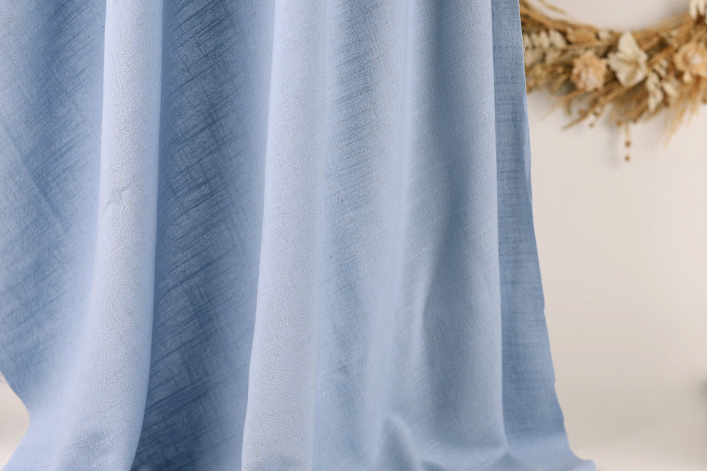 a close-up view of a light blue fabric, possibly a curtain or textile, with a wreath of dried flowers in the background.