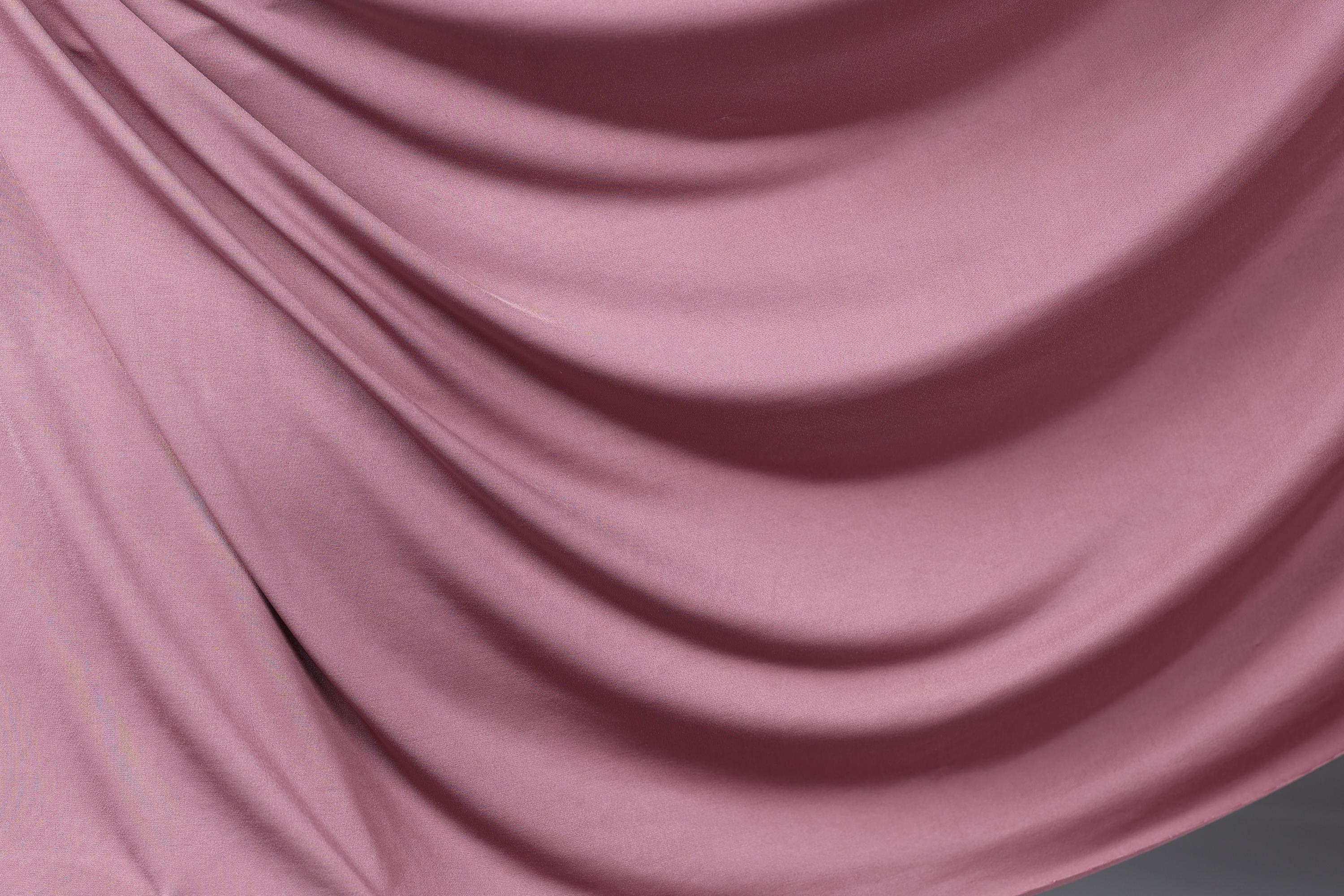 a close-up view of a soft, flowing pink fabric, possibly silk or satin, with a smooth, shiny texture.