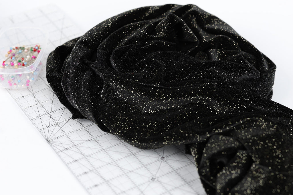 a black fabric with a glittery texture, placed on a white surface next to a clear plastic container filled with colorful pins.