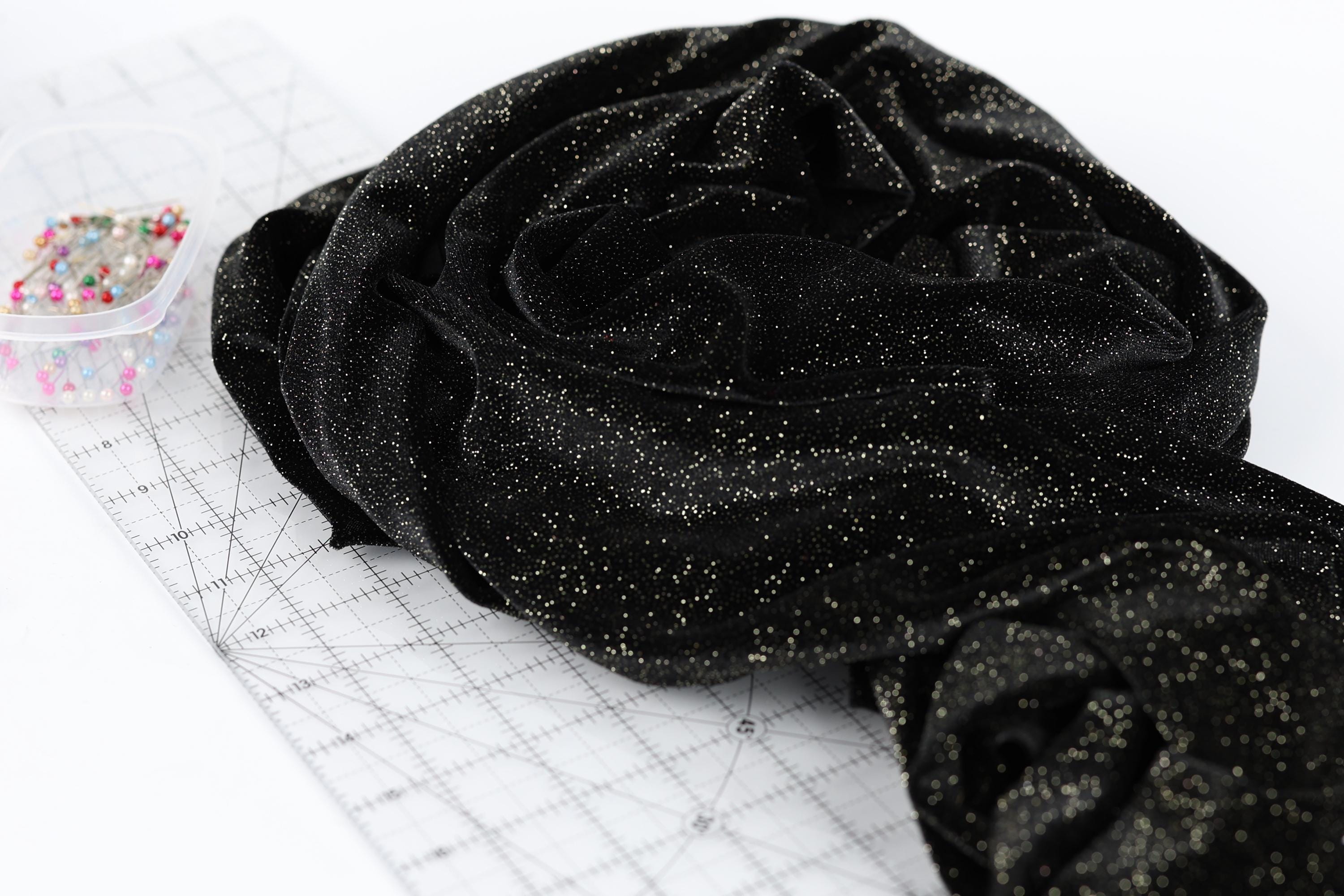 a black fabric with a glittery texture, placed on a white surface next to a clear plastic container filled with colorful pins.