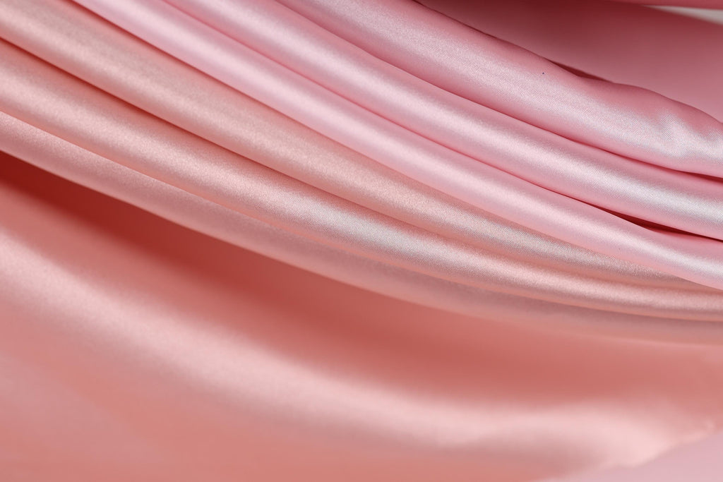 A close-up view of a soft, flowing pink fabric, possibly silk or satin, with a smooth and shiny texture.