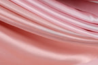 A close-up view of a soft, flowing pink fabric, possibly silk or satin, with a smooth and shiny texture.