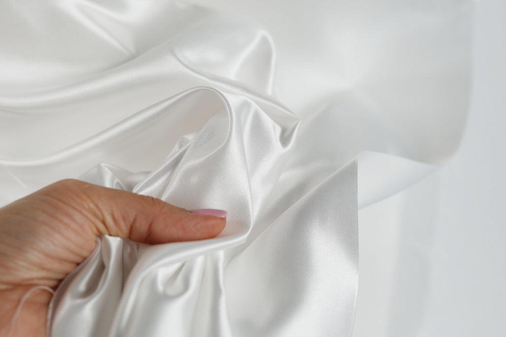 A hand is holding a piece of white satin fabric, with the fabric appearing to be wrinkled.