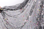 a close-up view of a delicate, intricately embroidered fabric with a floral pattern. The fabric appears to be made of sheer material, giving it a soft and delicate appearance. The embroidery features a variety of flowers and leaves in different colors, creating a visually appealing and detailed design.