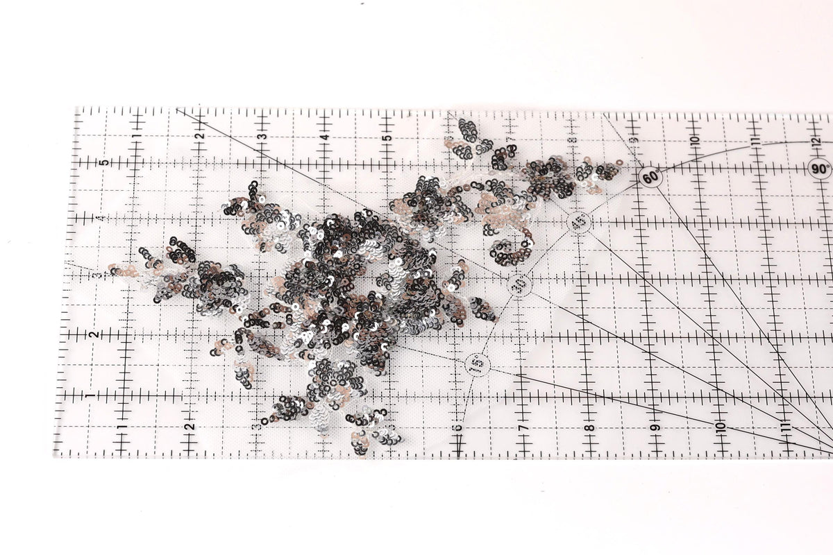 a collection of sequin pieces scattered on a transparent ruler, which is placed on a white surface.