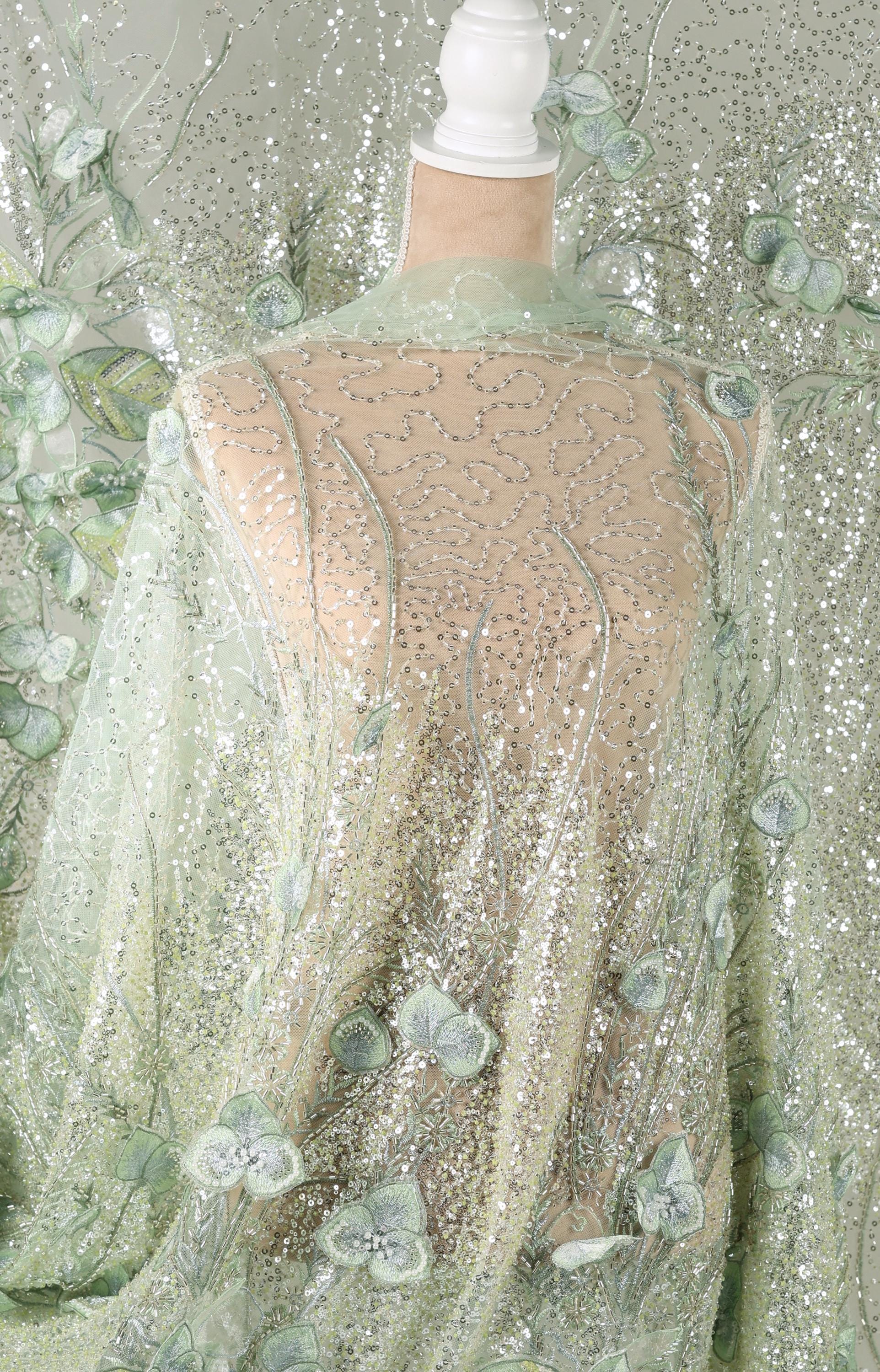 a mannequin wearing a sheer, mint green fabric with a floral pattern. The fabric appears to be made of sheer lace or sheer mesh, with a delicate, embroidered design. The mannequin is positioned in front of a background that is also covered in a similar mint green fabric with a floral pattern, creating a cohesive and visually appealing display.