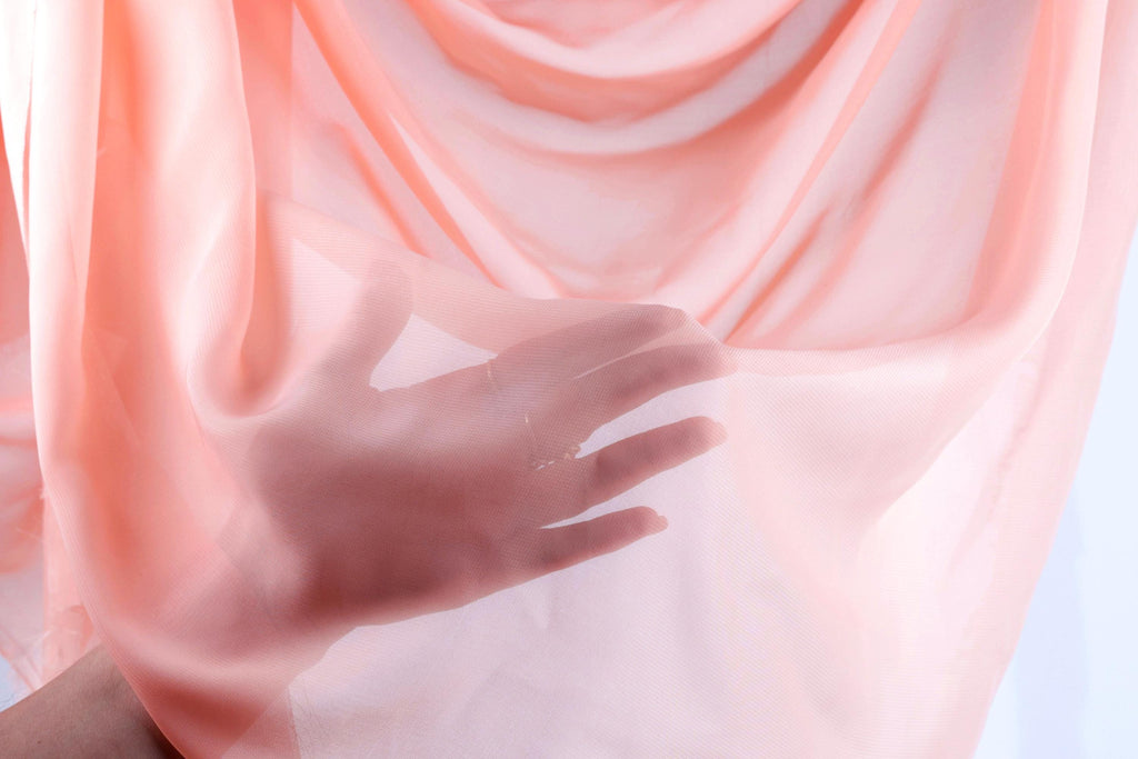 A hand is holding a piece of pink fabric, which appears to be a sheer or sheer-like material.