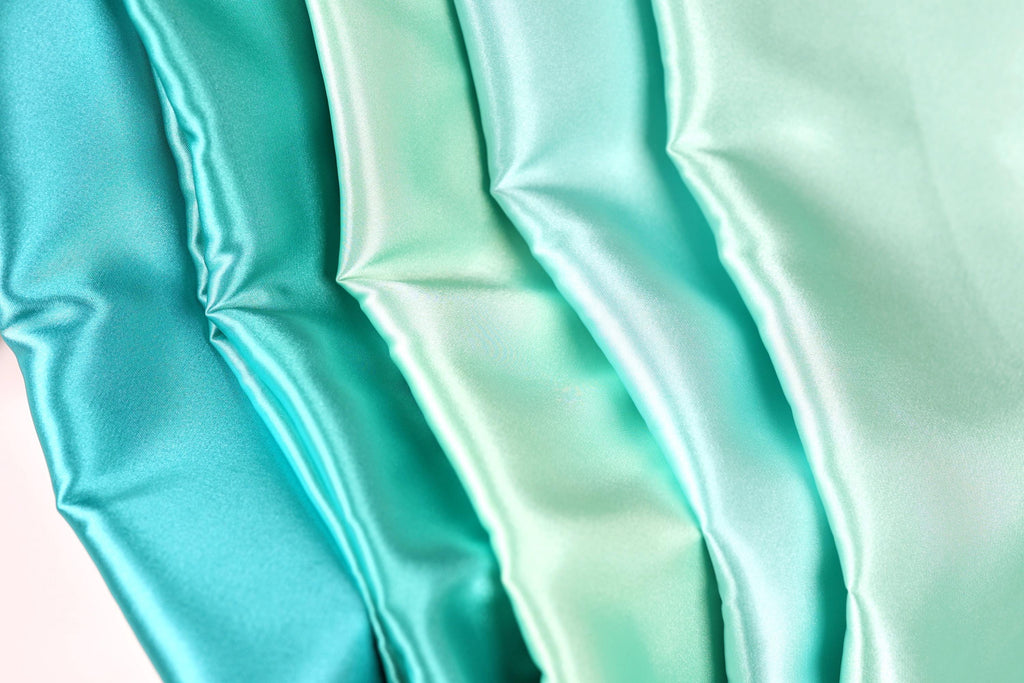 A close-up image of a fabric with a gradient of turquoise to mint colors, creating a visually appealing and vibrant pattern.