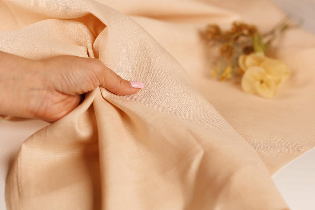 A hand is holding a piece of fabric, with a blurred bouquet of flowers in the background.