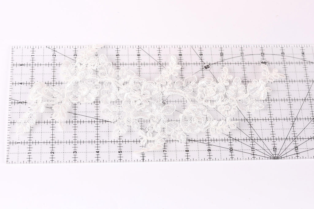 a close-up view of a piece of white lace with intricate floral patterns, placed on a transparent ruler.