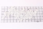 a close-up view of a piece of white lace with intricate floral patterns, placed on a transparent ruler.