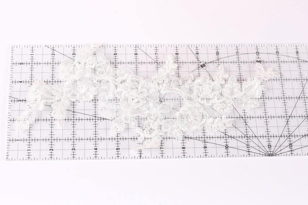 a close-up view of a piece of white lace with intricate floral patterns, placed on a transparent ruler.
