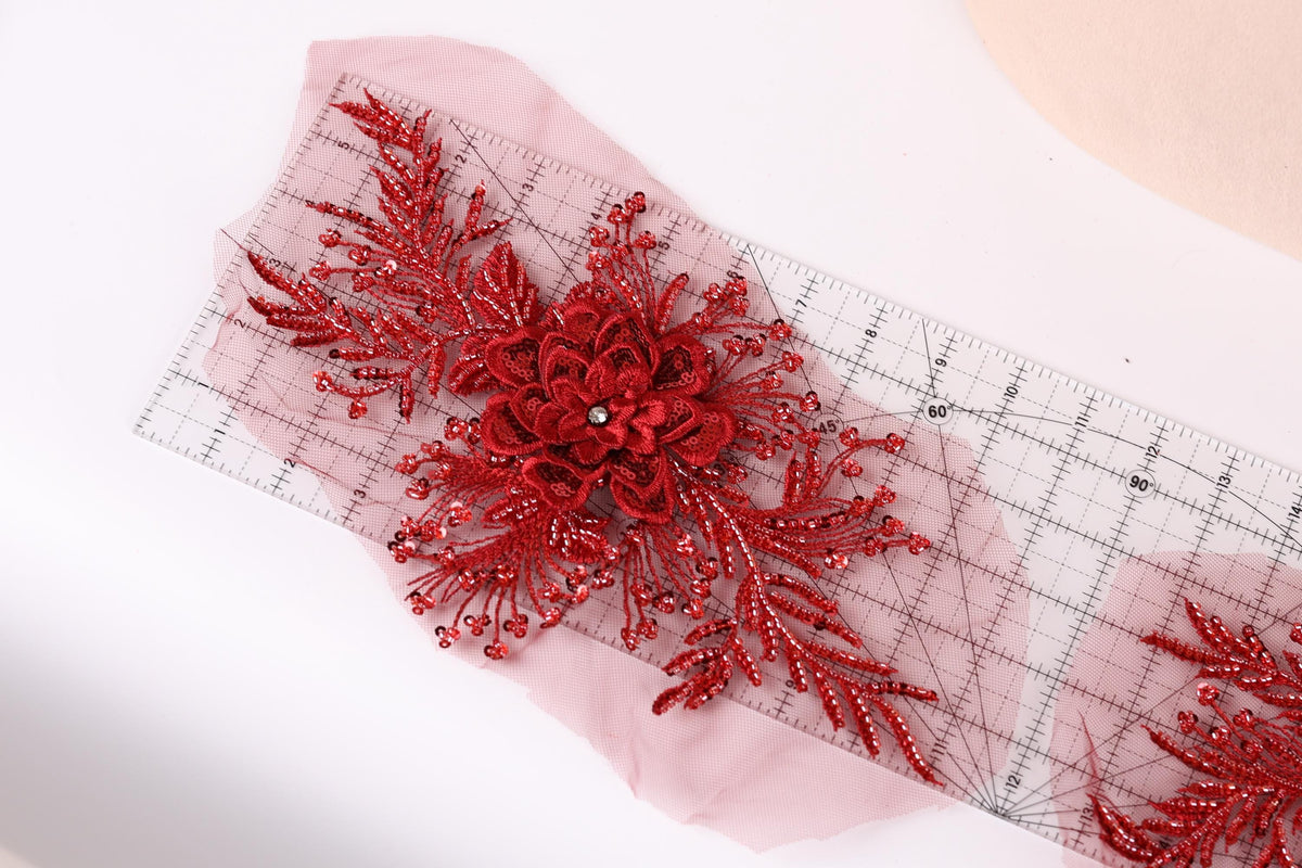 a close-up view of a red floral embellishment with a large flower at its center, surrounded by smaller red flowers and leaves. The embellishment is placed on a transparent surface, allowing the viewer to see the intricate details.