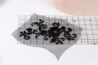 a piece of black lace with intricate floral patterns, placed on a transparent surface. A ruler is visible in the background, indicating that the lace may be used for a sewing or crafting project.