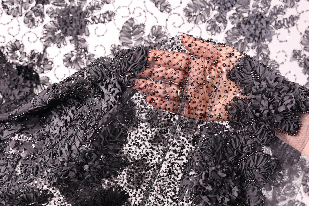 A close-up view of a hand holding a piece of black fabric with a floral pattern, featuring small black beads or sequins.