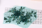 a pair of green sequin flowers on a light blue background, with a ruler placed in the foreground to measure the size of the flowers.