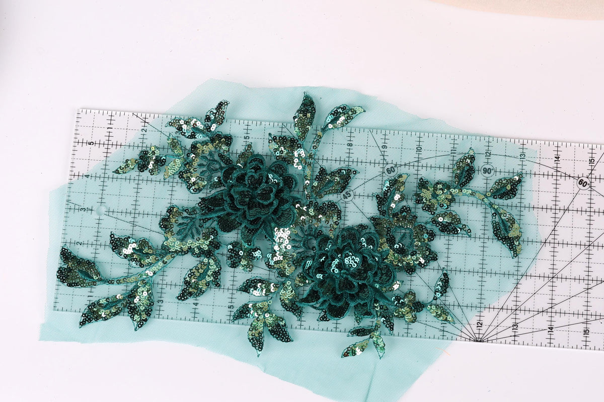 a pair of green sequin flowers on a light blue background, with a ruler placed in the foreground to measure the size of the flowers.