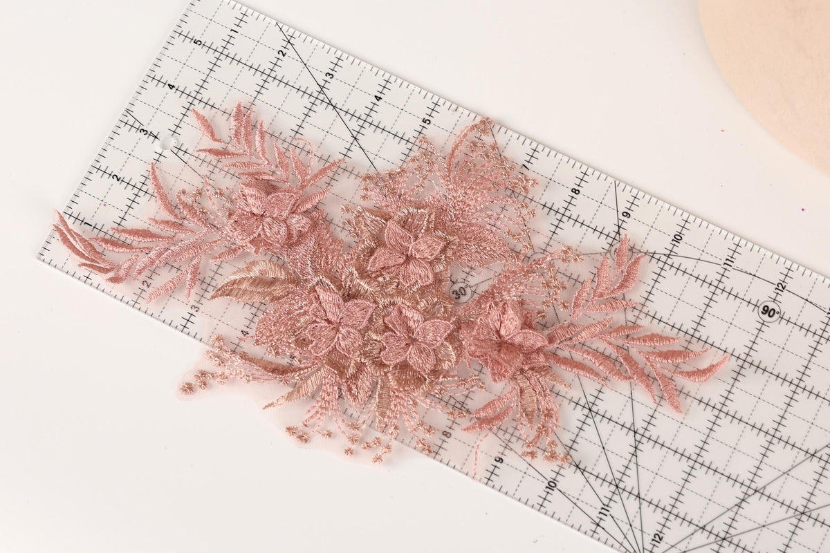 a close-up view of a clear ruler with pink floral embroidery attached to it.