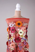 A mannequin wearing a vibrant red dress with a variety of colorful flowers and floral patterns.