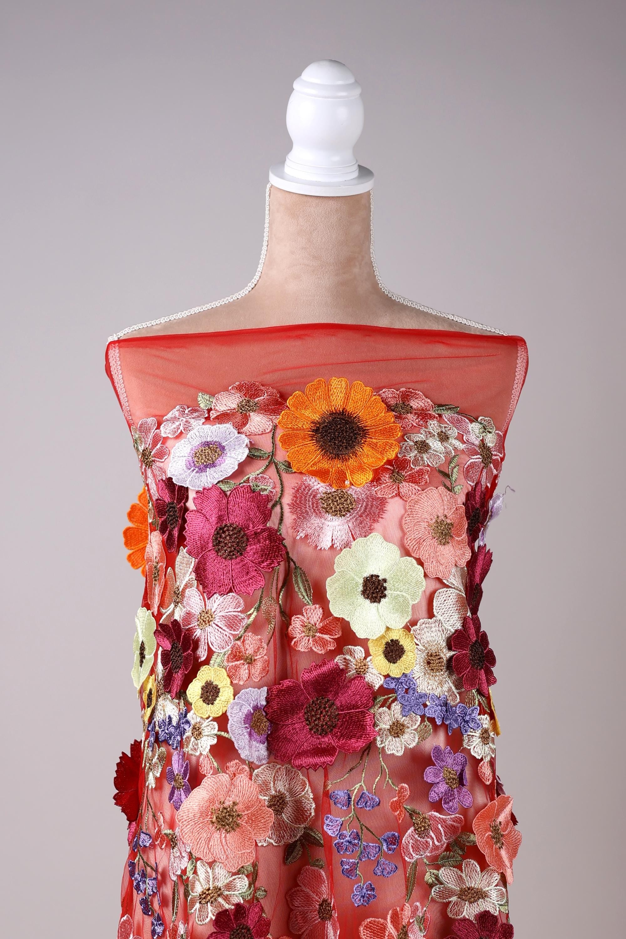 A mannequin wearing a vibrant red dress with a variety of colorful flowers and floral patterns.