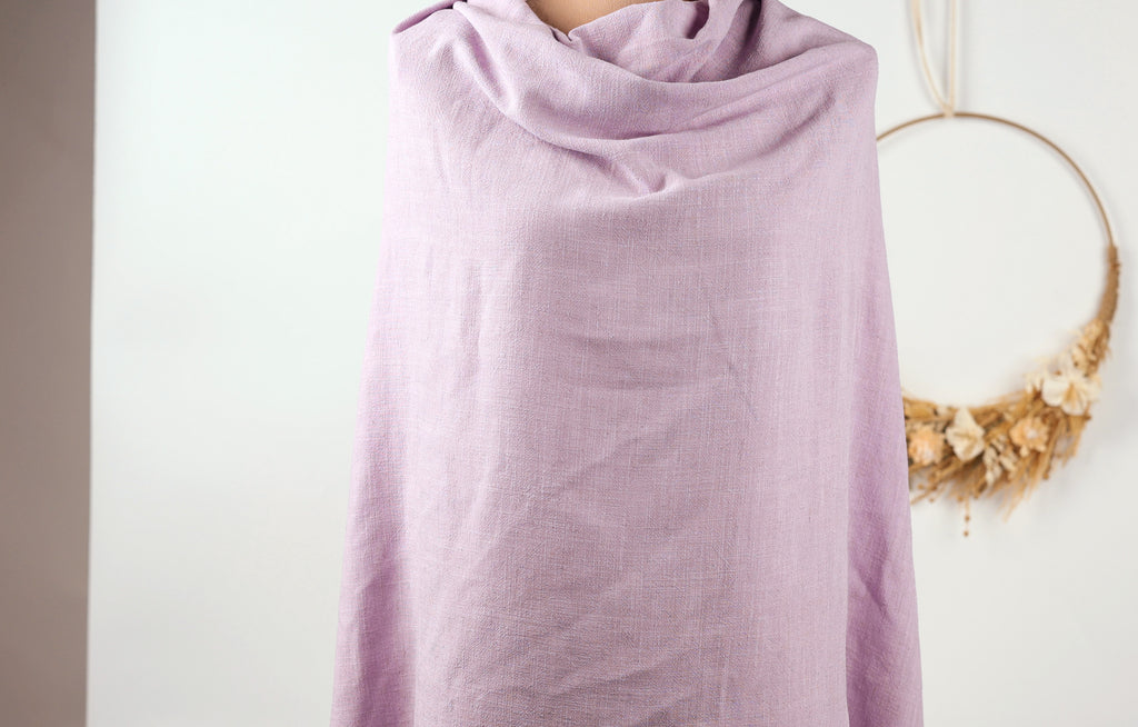 A person is standing in front of a white wall, wearing a purple scarf.