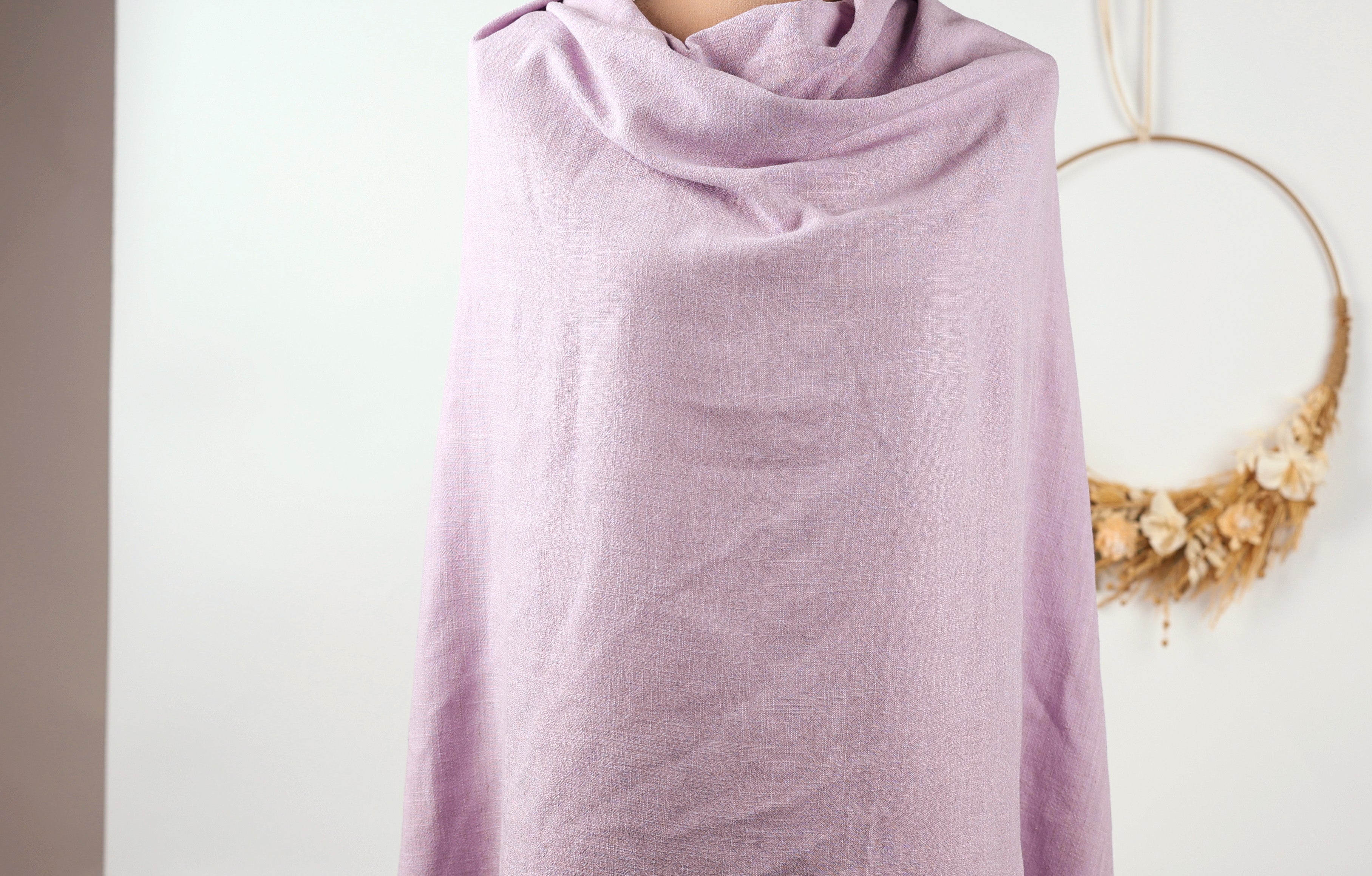 A person is standing in front of a white wall, wearing a purple scarf.