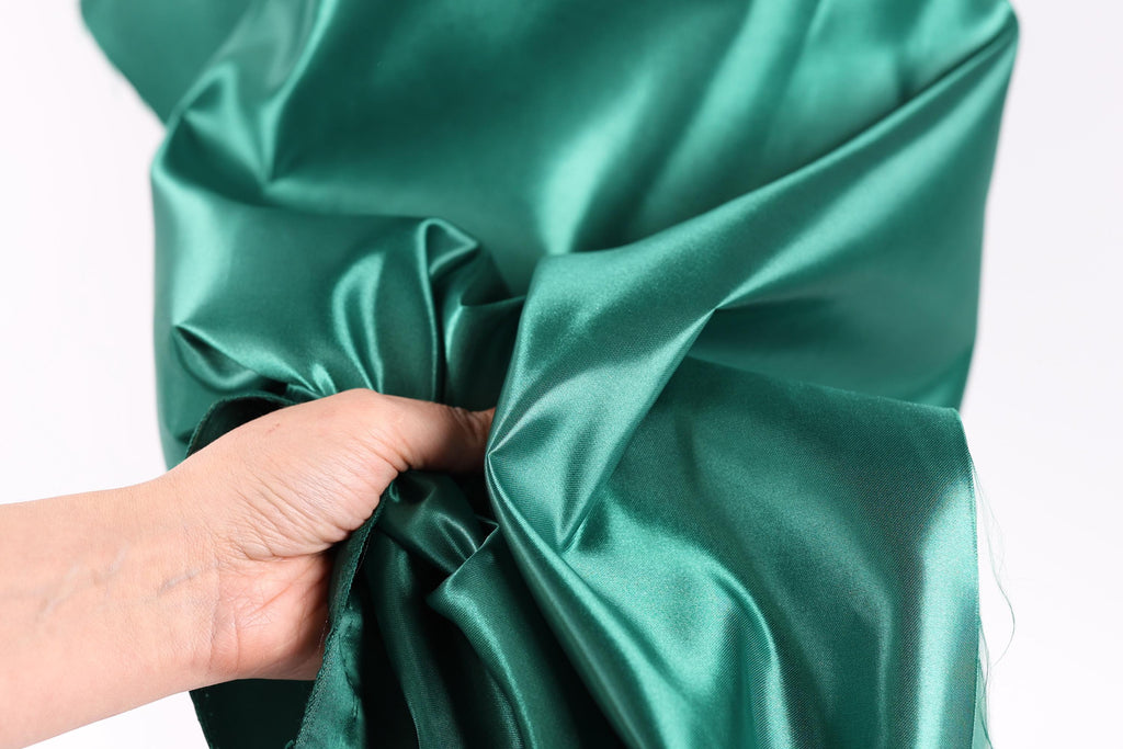 A hand is holding a piece of green satin fabric, which appears to be a close-up view of the material.