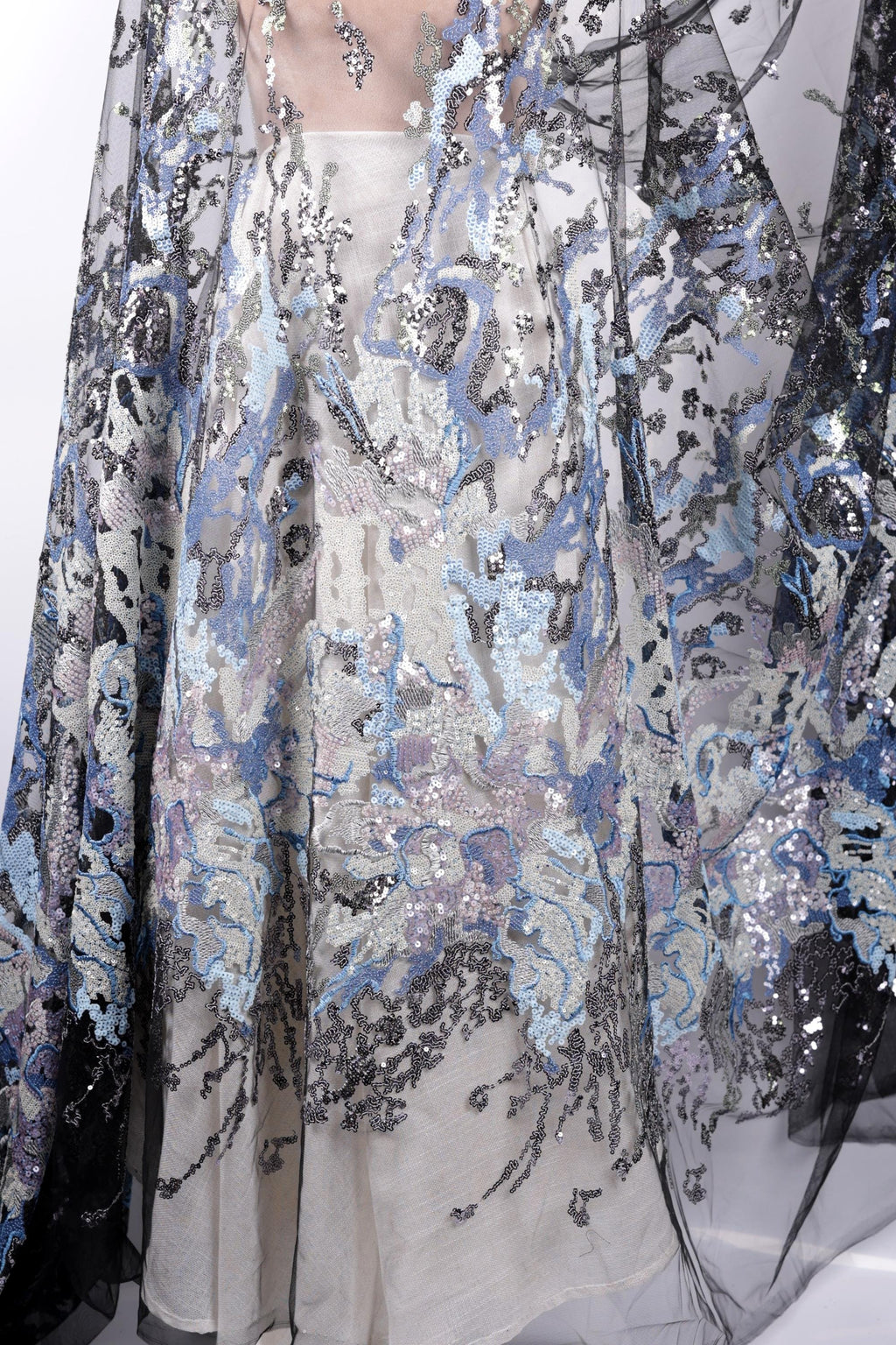 a close-up view of a fabric with a floral pattern and sequin details. The fabric appears to be a sheer material, with a mix of blue, gray, and black colors. The pattern is intricate and detailed, showcasing the craftsmanship of the fabric.