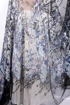 a close-up view of a fabric with a floral pattern and sequin details. The fabric appears to be a sheer material, with a mix of blue, gray, and black colors. The pattern is intricate and detailed, showcasing the craftsmanship of the fabric.