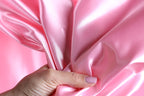 A hand is holding a piece of pink satin fabric, with the fabric partially draped over the hand.