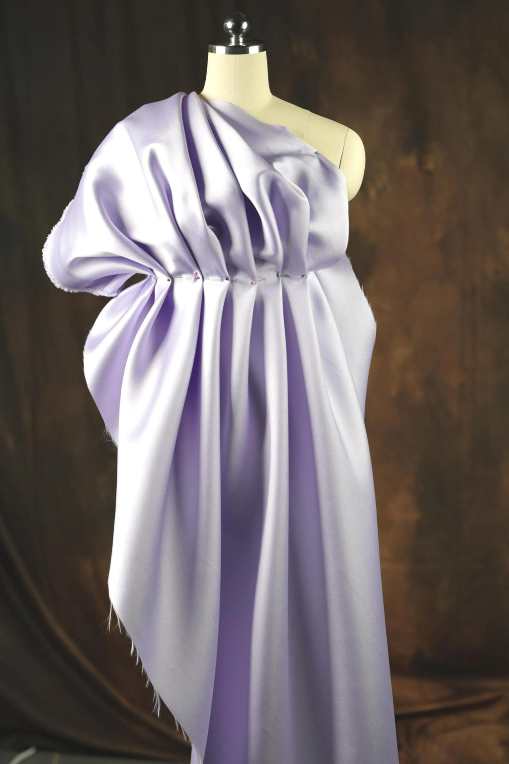 A close-up view of a purple fabric draped over a mannequin head, creating a flowing, draped effect.