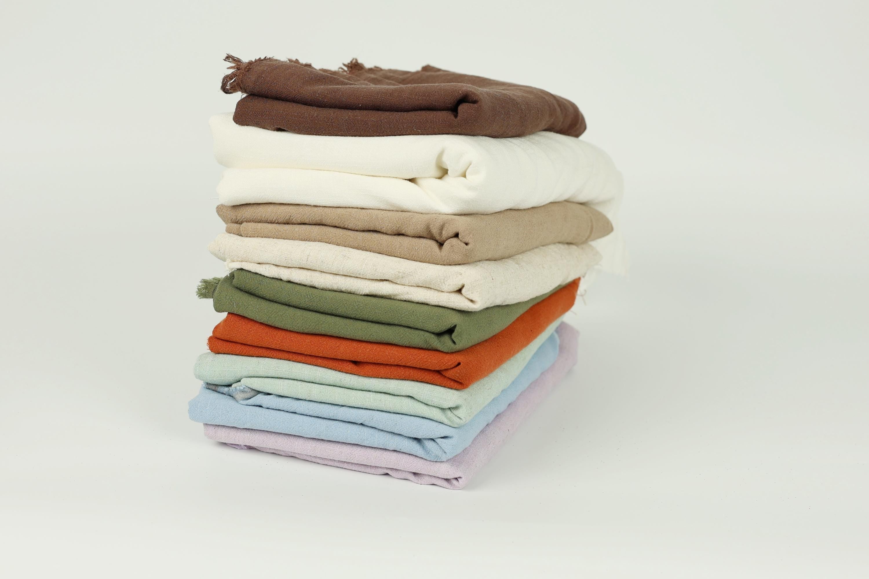 A stack of various colored towels or cloths, including white, brown, green, orange, and blue, arranged in a visually appealing manner.