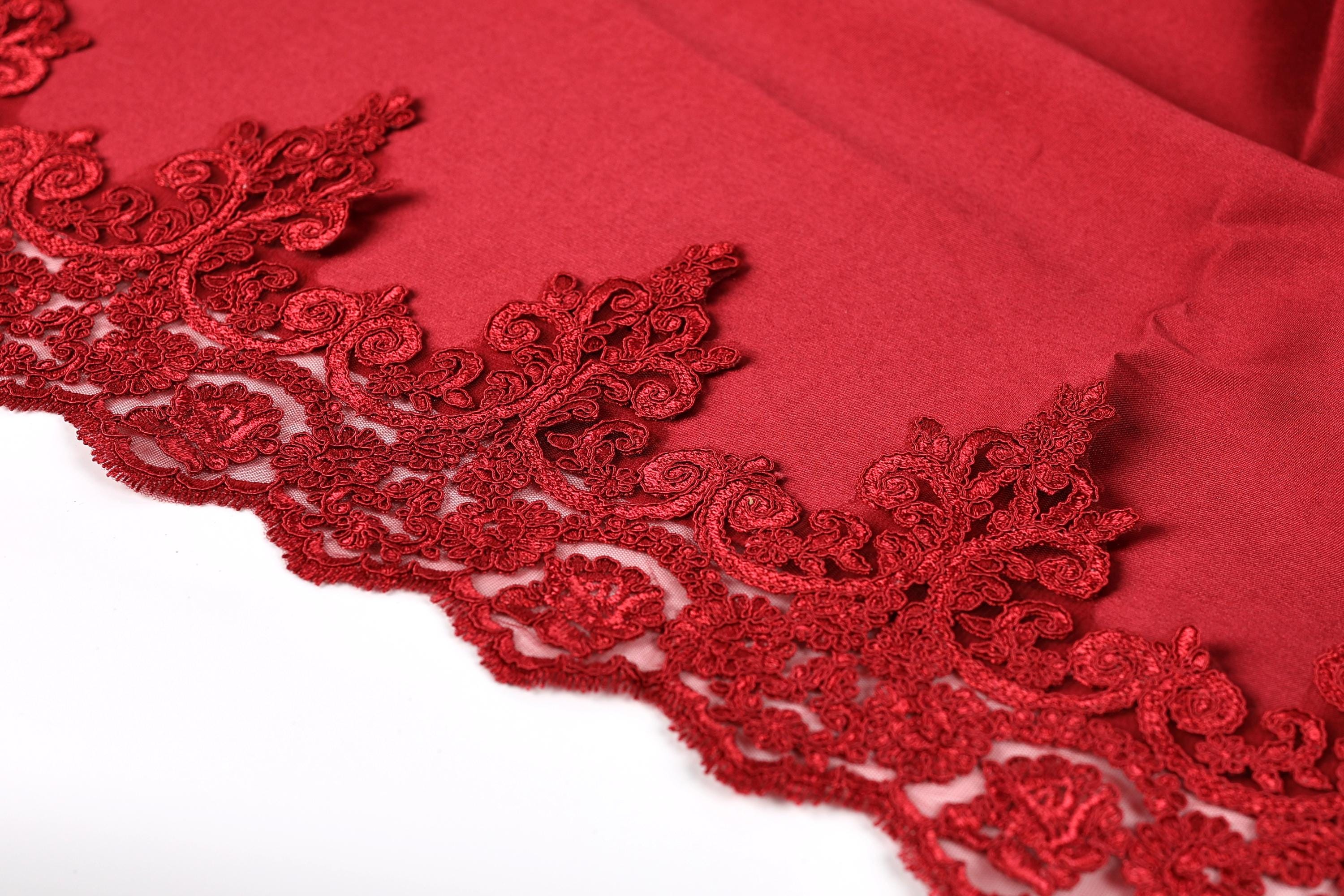 a close-up view of a red fabric with intricate red lace-like patterns along the edge, creating a visually striking and elegant design.