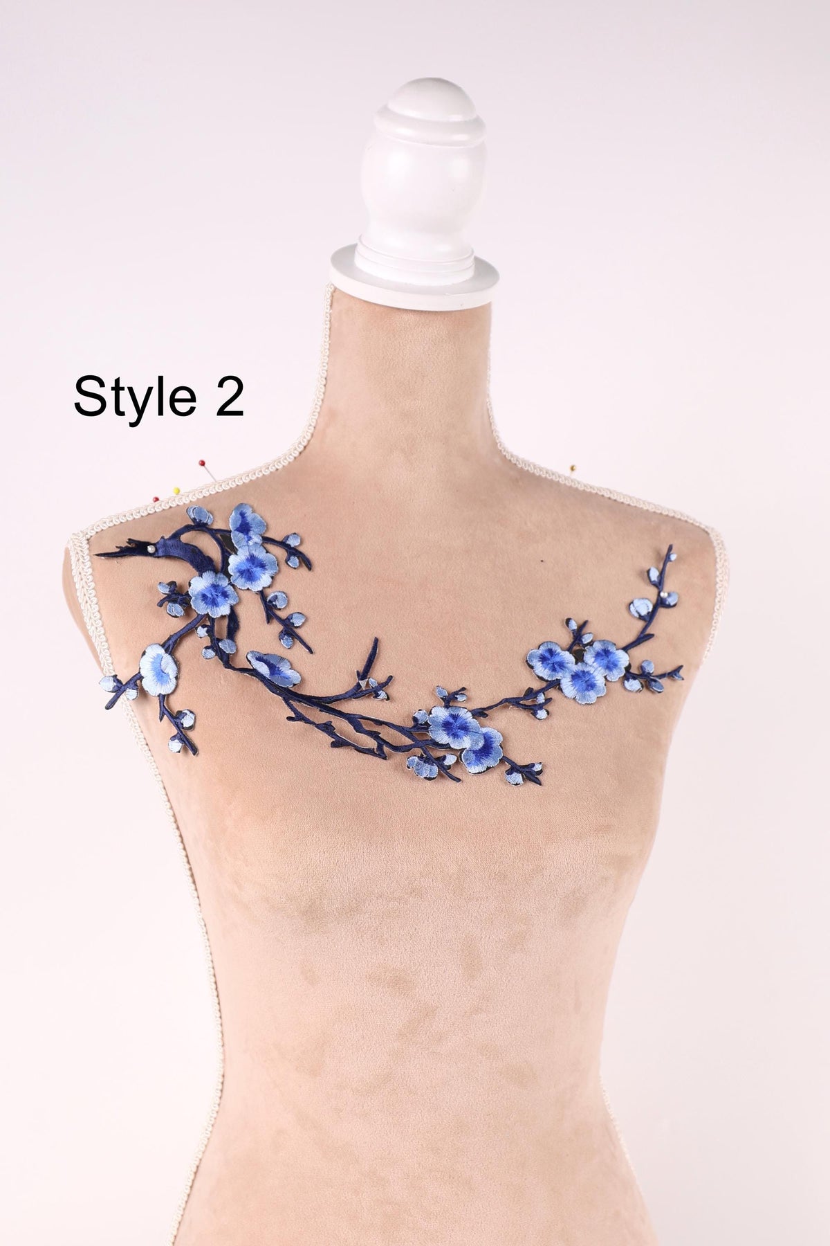 A mannequin with a floral embroidered design on its shoulder, featuring blue flowers and branches.