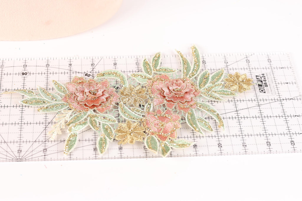 a decorative floral lace piece with pink and green flowers and leaves, placed on a ruler for scale.