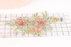a decorative floral lace piece with pink and green flowers and leaves, placed on a ruler for scale.