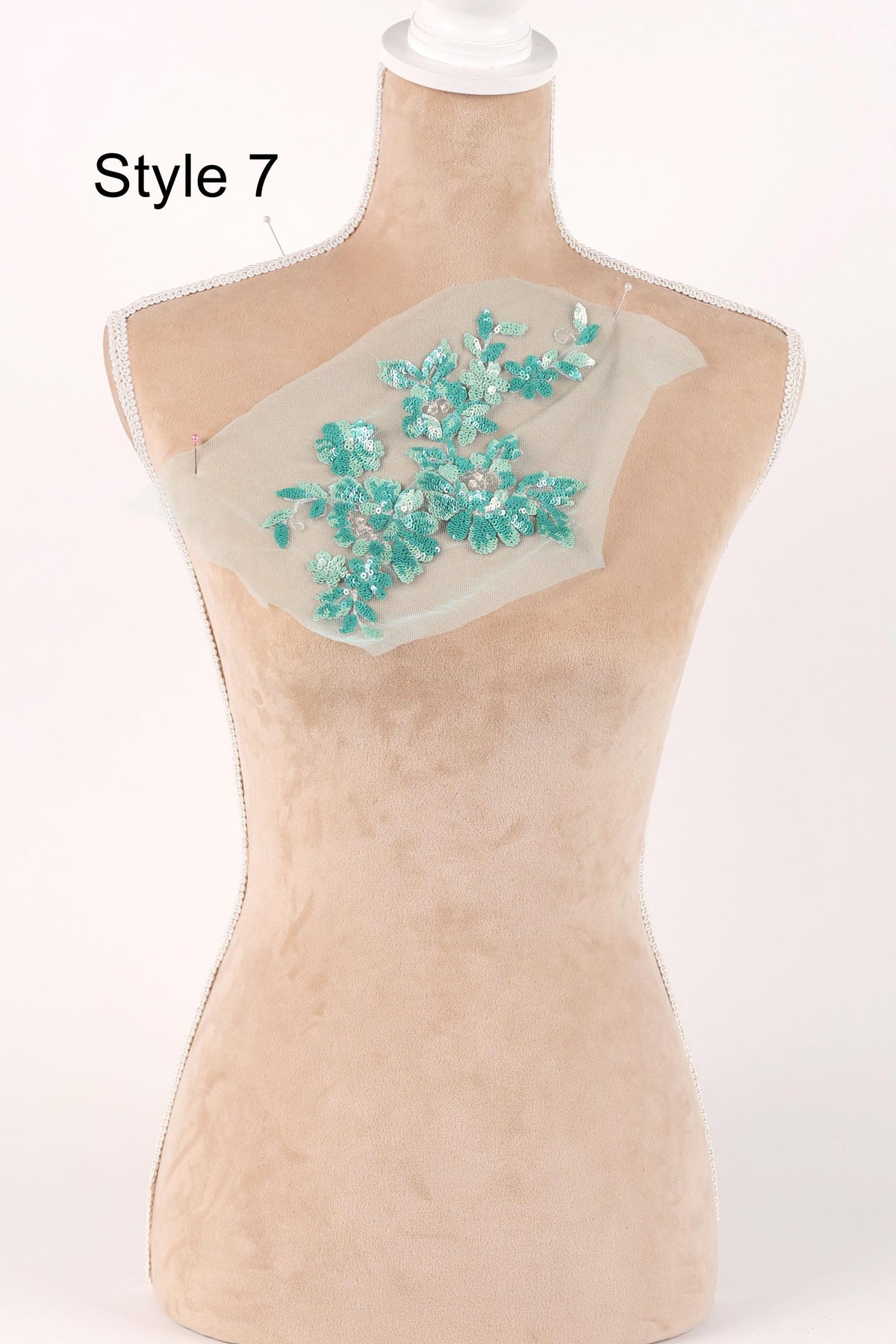 A mannequin with a beige body and a white head, wearing a beige dress with a green floral embroidered on the chest area.