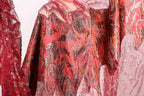a close-up view of a vibrant red and pink fabric with intricate patterns and designs, including a floral motif and sparkling embellishments.