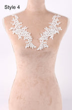 A mannequin wearing a beige dress with white lace floral appliques on the shoulders.