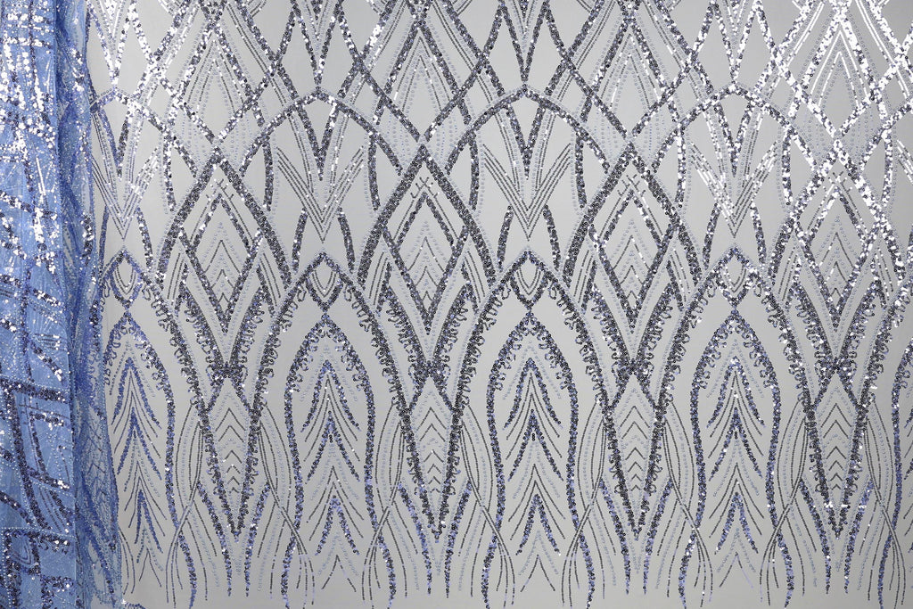 a close-up view of a fabric with a repeating pattern of silver and blue sequin designs. The pattern consists of a series of arched shapes and lines that create a visually striking and intricate design. The fabric appears to be a type of sheer material, with the silver and blue sequins adding a touch of sparkle and elegance to the overall appearance.