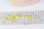 a clear ruler with yellow flower-shaped cutouts placed on it, creating a decorative arrangement.
