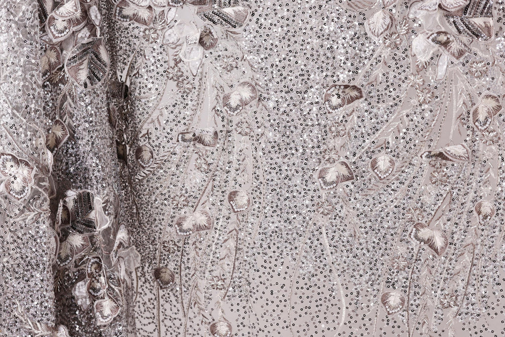 The image is a close-up of a fabric with a floral pattern, featuring a mix of small white and gray sequins and flowers.