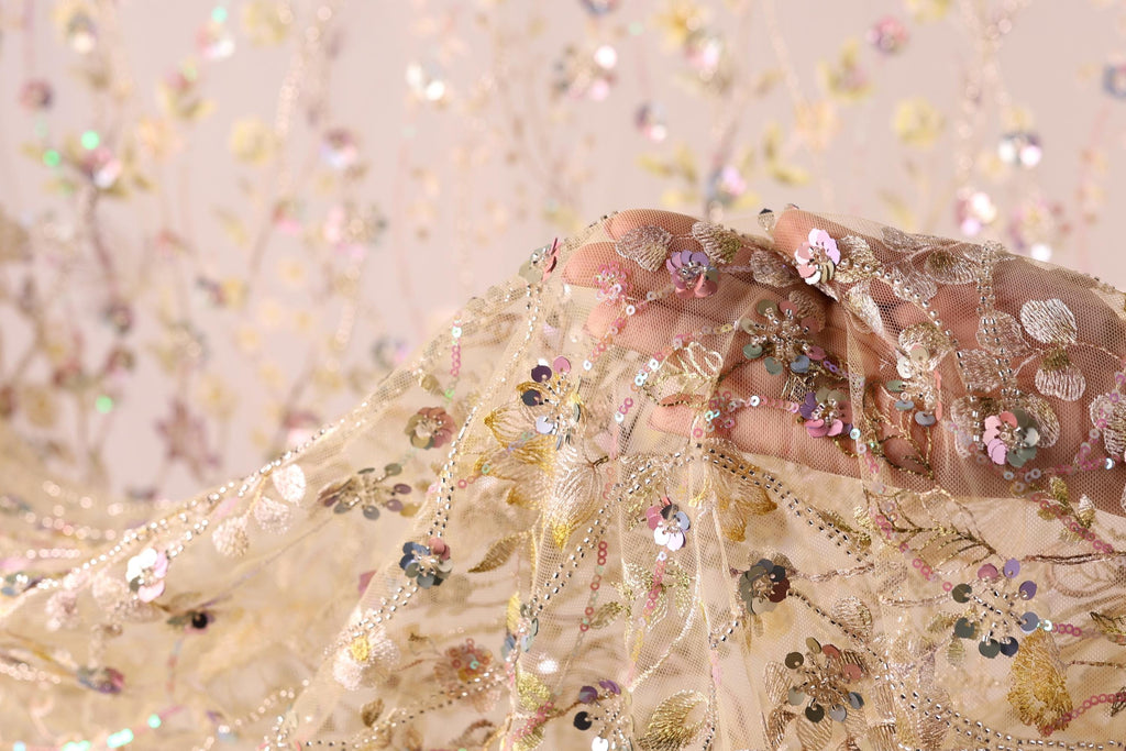 A hand is holding a delicate, intricately embroidered fabric with a floral pattern.