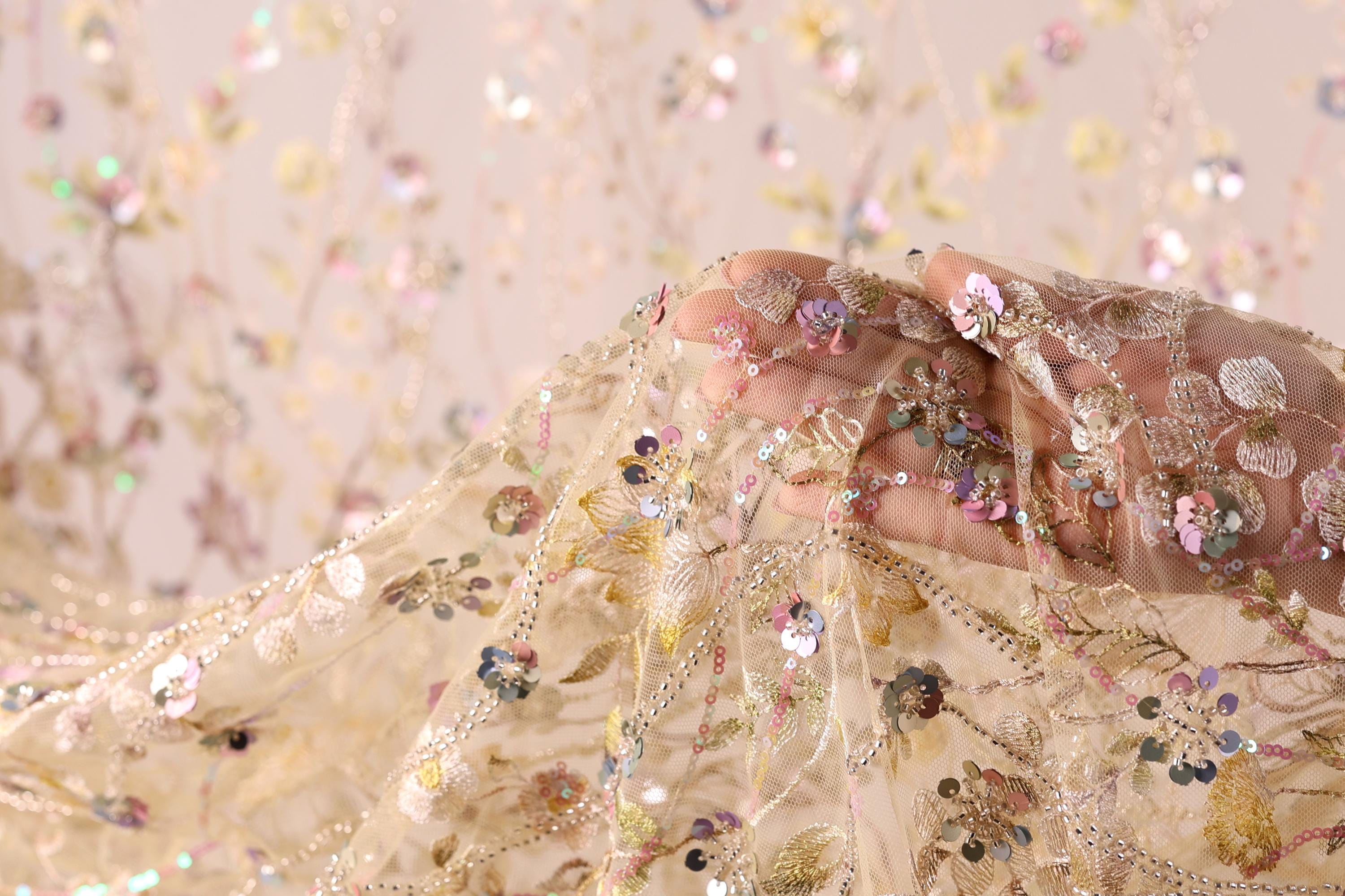 A hand is holding a delicate, intricately embroidered fabric with a floral pattern.