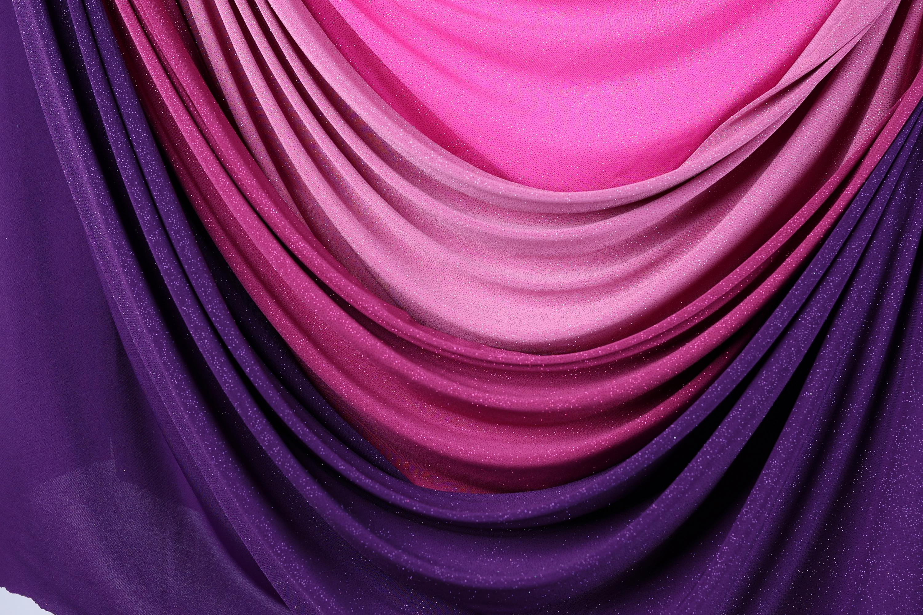 a close-up view of a fabric with a gradient of colors, transitioning from purple to pink and then to a darker shade of pink. The fabric appears to be made of a shiny, glittery material, adding a touch of sparkle to the overall appearance.