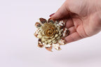 A hand holding a decorative flower-shaped object with sequin details against a plain background.