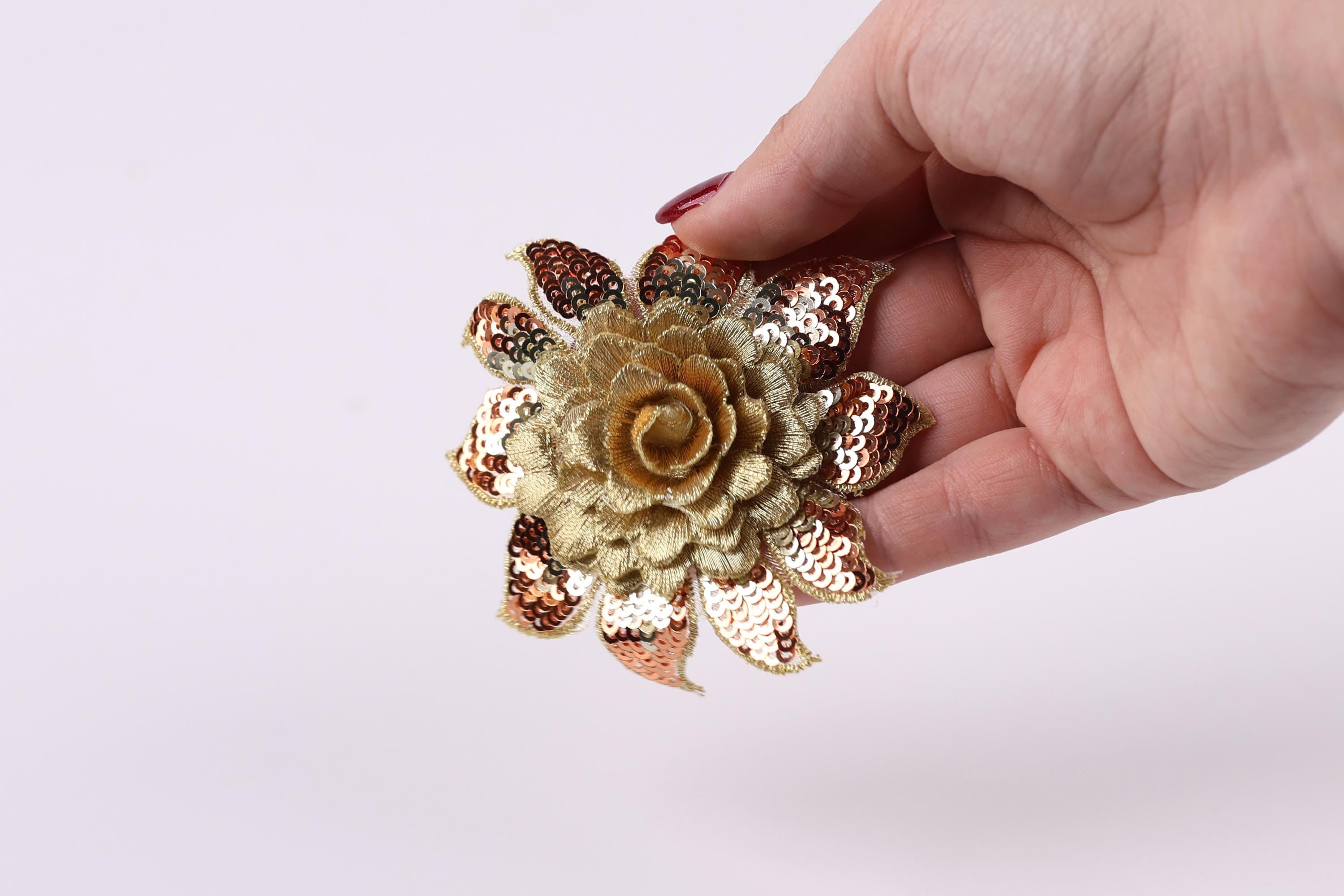 A hand holding a decorative flower-shaped object with sequin details against a plain background.
