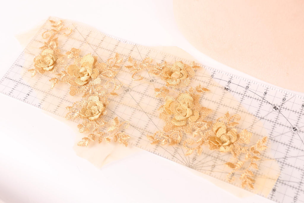 a close-up view of a piece of fabric with gold embroidered flowers on it, placed on a transparent surface.