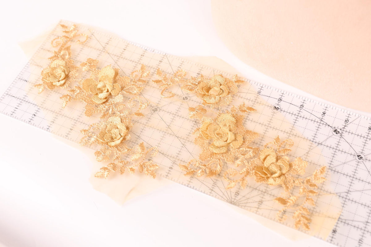 a close-up view of a piece of fabric with gold embroidered flowers on it, placed on a transparent surface.