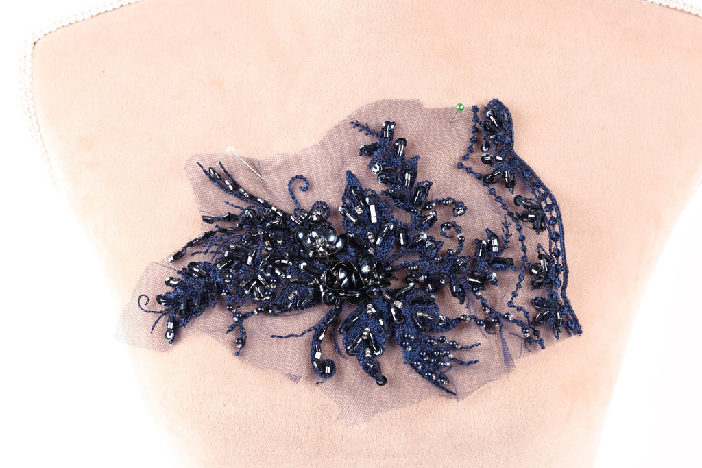 a close-up view of a piece of fabric with a decorative element, possibly a lace or embroidery piece, featuring a variety of blue and black beads or sequins.